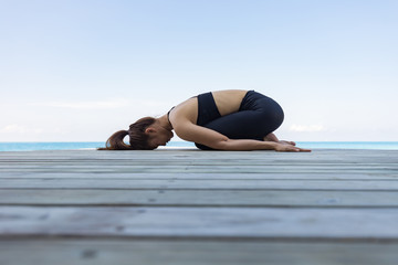 Fototapeta na wymiar Asian woman wearing black sportswear relaxing in yoga Child's Pose stretching exercises muscle for warm up on beach in Maldives with seaside,Feeling so comfortable and relax in holiday,Healthy Concept