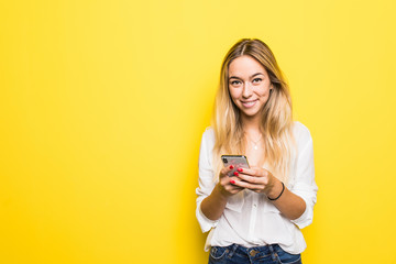 Portrait of young girl holding mobile phone while standing isolated over yellow background