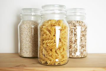 Various uncooked cereals, grains, and pasta for healthy cooking in glass jars on wooden table. Top view. Clean eating, balanced dieting food