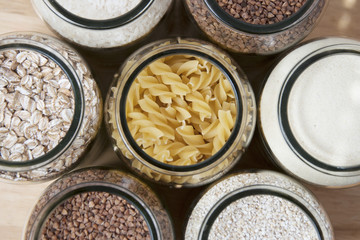 Various uncooked cereals, grains, and pasta for healthy cooking in glass jars on wooden table. Top view. Clean eating, balanced dieting food