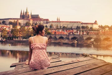 Cercles muraux Prague Young woman sitting on wood pier looking Prague Castle, Prague river Vltava and many famous Prague sights and historic architecture, back view.