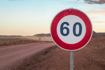 A speed limit sign in the middle of a desertic dirt road, in Morocco, Africa. Behind a sand storm...