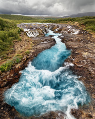 Scenic view of a waterfall with blue coloring, in the background a mountain range - Location: Iceland, Golden circle