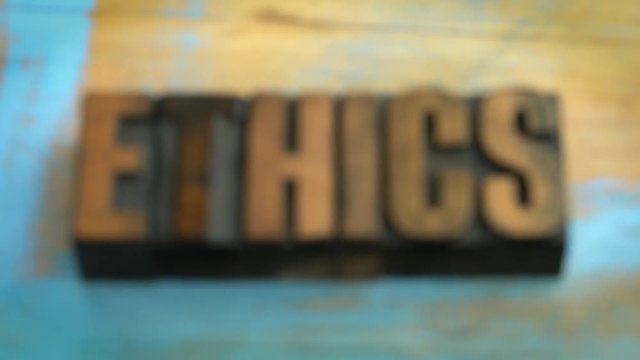 Ethics - rack focus on a word in vintage letterpress wood type printing blocks (inverted) against grange wooden board with a cup of coffee