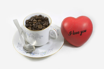 Close up of a white cup of coffee full of coffee beans and a red heart on white background. Concept: Love, relax, Flaver