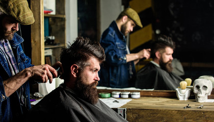 Barber styling hair of bearded client with comb and clipper. Barber with hair clipper works on...