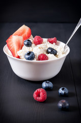 Curd with blueberries and raspberries in a white plate on a black wooden background