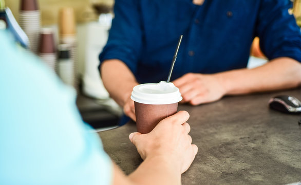 Served in paper cup coffee to go. Hand of barista at bar serve coffee for client. Hand gives cup to client visitor. Enjoy your drink. Man receive drink at bar counter. Cappuccino or cacao with straw