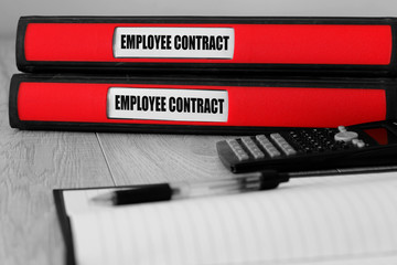 Red folders with employee contract written on the label on a desk with selective colour