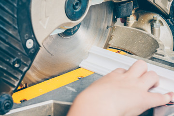 The boy cuts the ceiling polystyrene foam plinth with a crosscut saw