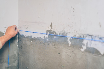 finishing works - the worker makes a marking with chalk with the help of a padded cord on the wall