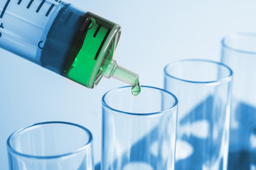Syringe dropping a chemical solution into a test tube on soft light background.