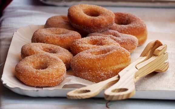 Donuts with sugar on a tray in a bar., On the right a rustic wooden cake tongs  to serve them.