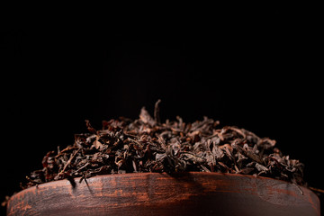 Top view of dried black tea in clay bowl on wooden table. Concept of tea production. Macro, close up