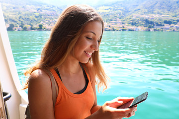 Cruise ship woman using mobile phone on travel vacation. Girl texting sms or using Wifi Internet. Tourist looking at her holidays pictures.
