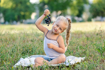 Fototapeta premium cute little girl eating grapes in the park