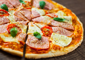 sliced Pizza with Mozzarella cheese, Ham, Tomatoes, pepper, Spices and Fresh Basil. Italian pizza on wooden background