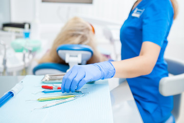 A close-up photo of a dentist's hand taking a sterile instrument from a metal tray. Focus on the doctor's hand