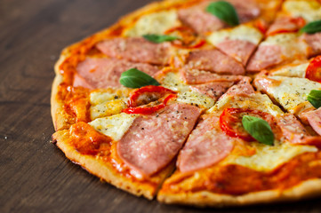 sliced Pizza with Mozzarella cheese, Ham, Tomatoes, pepper, Spices and Fresh Basil. Italian pizza on wooden background