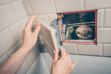 The girl opens a hidden hatch on the wall of the tile to access the inspection hole of the sewer pipe to eliminate clogging and cleaning