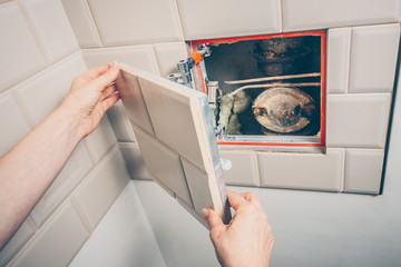 The girl opens a hidden hatch on the wall of the tile to access the inspection hole of the sewer pipe to eliminate clogging and cleaning