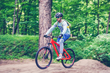 Fototapeta premium Cyclist in helmet on an orange bike doing a trick in a springboard jump in the forest, motion blur