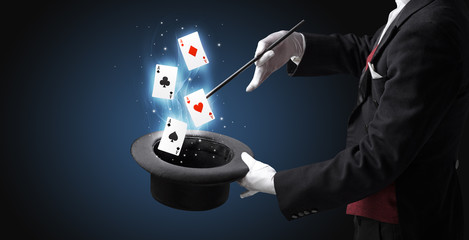 Magician with white gloves conjuring playing cards from a cylinder with magic wand © ra2 studio