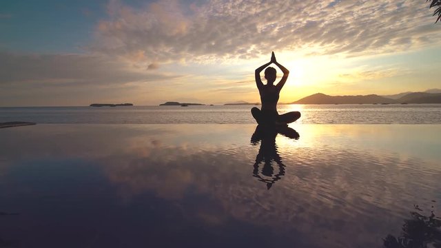 Silhouette of young woman practicing yoga on the resort pool at seashore with sunset background. Shot in 4k resolution