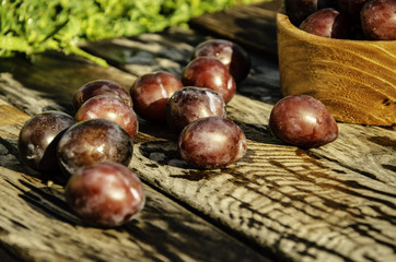 Vintage plums in a wooden bowl, on a wooden background, on the grass on a sunny afternoon on the grass.