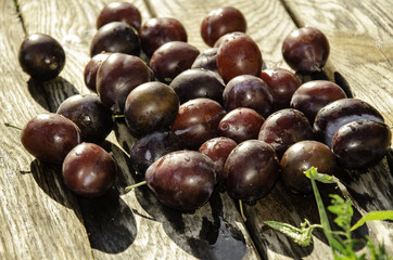 Vintage plums in a wooden bowl, on a wooden background, on the grass on a sunny afternoon on the grass.