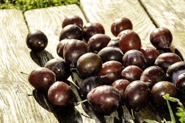 Vintage plums in a wooden bowl, on a wooden background, on the grass on a sunny afternoon on the grass.
