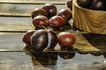 Vintage plums in a wooden bowl, on a wooden background, on the grass on a sunny afternoon on the grass.