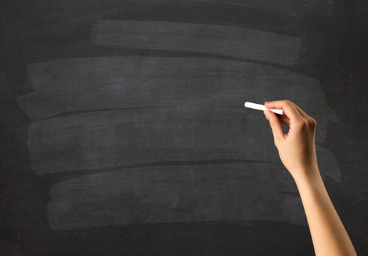 Female hand holding white chalk in front of a blank blackboard