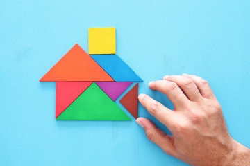 man's hand pointing at house made from tangram puzzle over wooden table