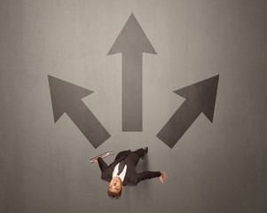 Young contemplating businessman stands in front of brown arrows