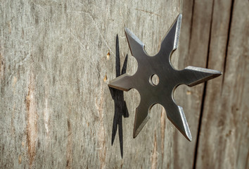 Shuriken (throwing star), traditional japanese ninja cold weapon stuck in wooden background © Sergii