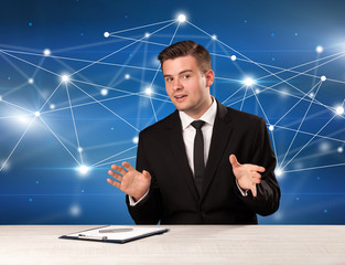 Young handsome businessman sitting at a desk with a blue connection graphic behnid him 
