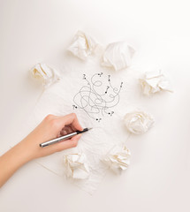 Female hand next to a few crumpled paper balls drawing random scribbles 