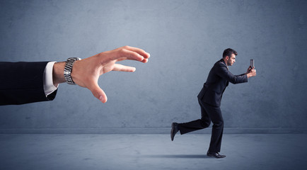 Young miniature businessman running from a big hand with blueish background