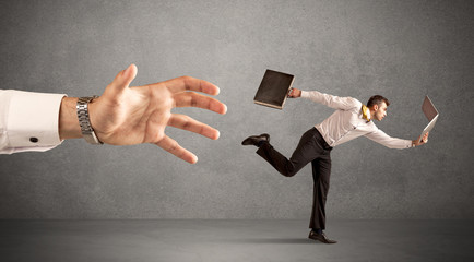 Young miniature businessman running from a big hand with light grey background