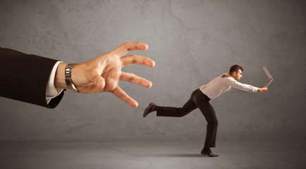 Young miniature businessman running from a big hand with grey background