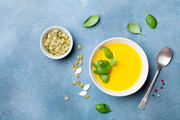 Autumn vegetable or pumpkin soup in white bowl on blue table top view.