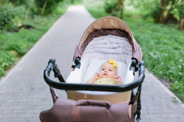 Cute little baby girl in yellow dress in brown baby carriage at outdoor, spring or summer season...