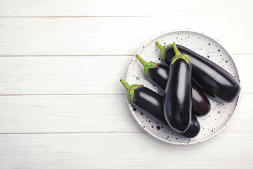 Plate with raw ripe eggplants on wooden background, top view