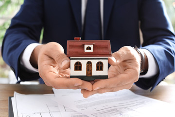Real estate agent holding house model at table in office, closeup
