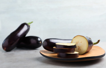 Wooden board with ripe eggplants on table