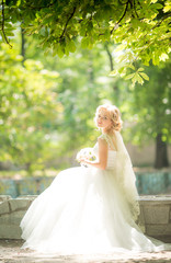 Beautiful blonde bride with stylish make-up in white dress with a wedding bouquet