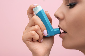 Young woman using asthma inhaler on color background, closeup - obrazy, fototapety, plakaty