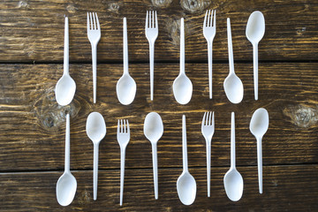 White plastic spoons and forks on a wooden background.