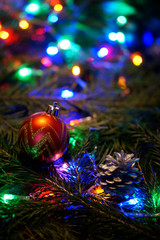 Obraz na płótnie Canvas A red golden ball and a lump on a tree branch among the multicolored lights. Congratulations on the New Year and Christmas. Vertical picture
